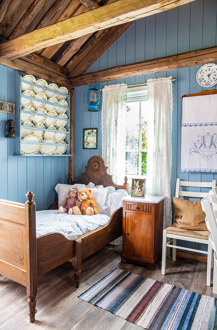 Children's room with antique wooden bed, blue-painted walls and shelf with porcelain plates