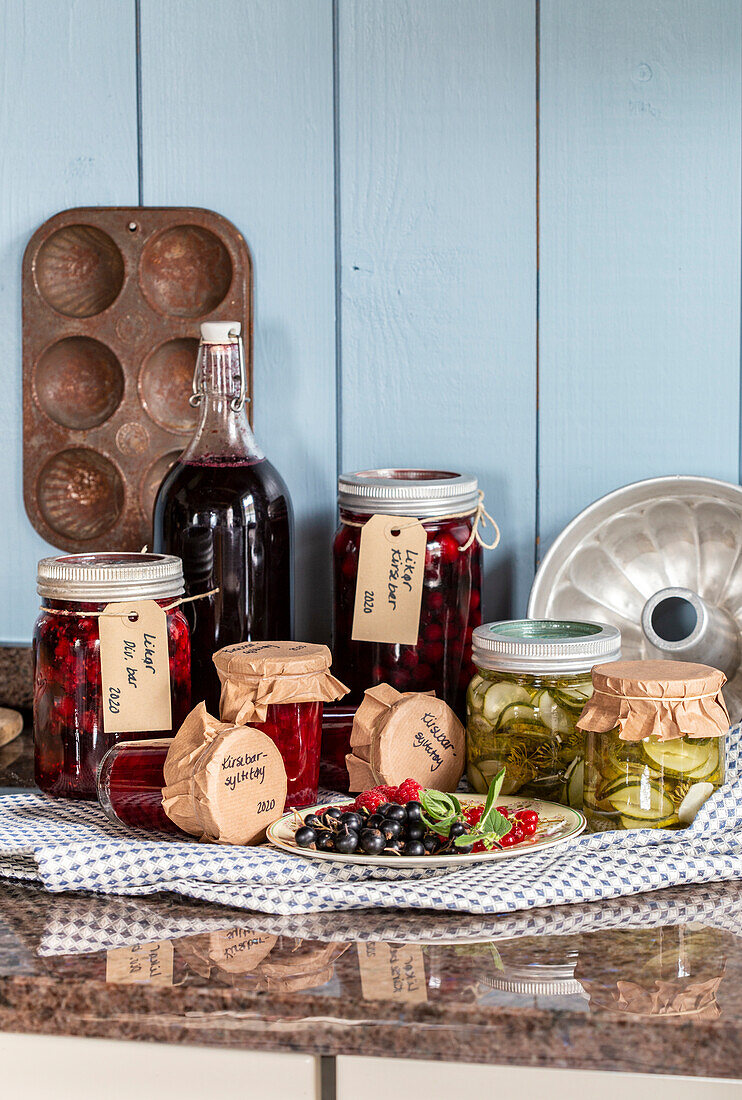 Homemade preserves and berries on kitchen worktop in front of blue wood panelling