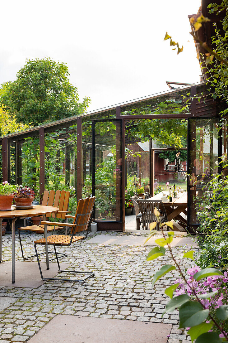 Glass-covered terrace, wooden furniture and plants in the summer garden