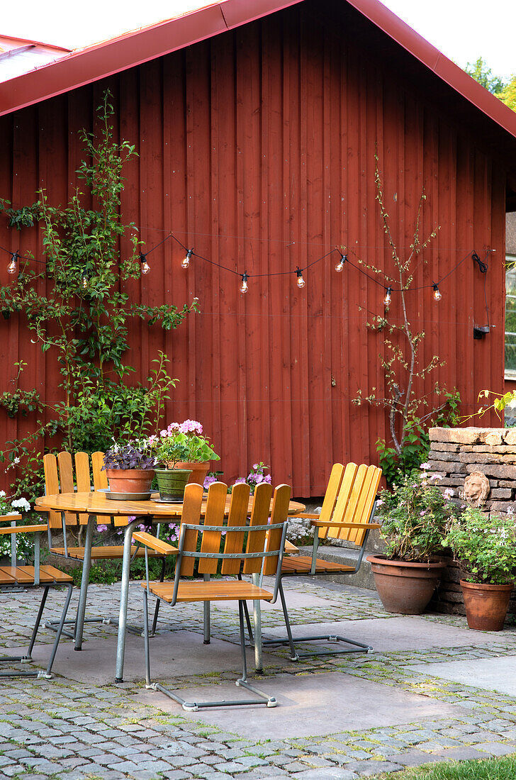 Garten-Sitzbereich mit Holzstühlen und Kübelpflanzen vor rotem Holzhaus