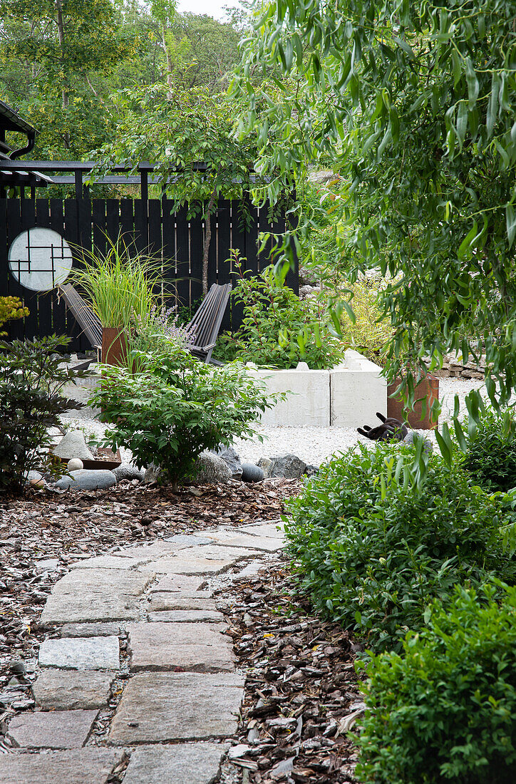 Garden path made of stone slabs leads to a modern seating area with privacy screen and lots of greenery