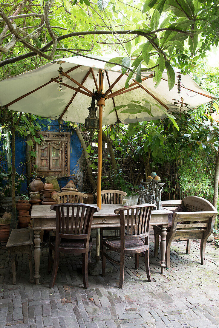 Rustikaler Holztisch mit Stühlen und Sonnenschirm im üppigen Garten