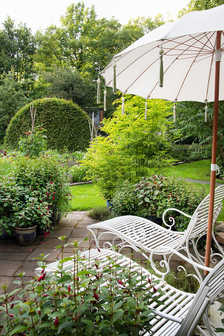 Zwei weiße Liegestühle mit Sonnenschirm auf der Gartenterrasse