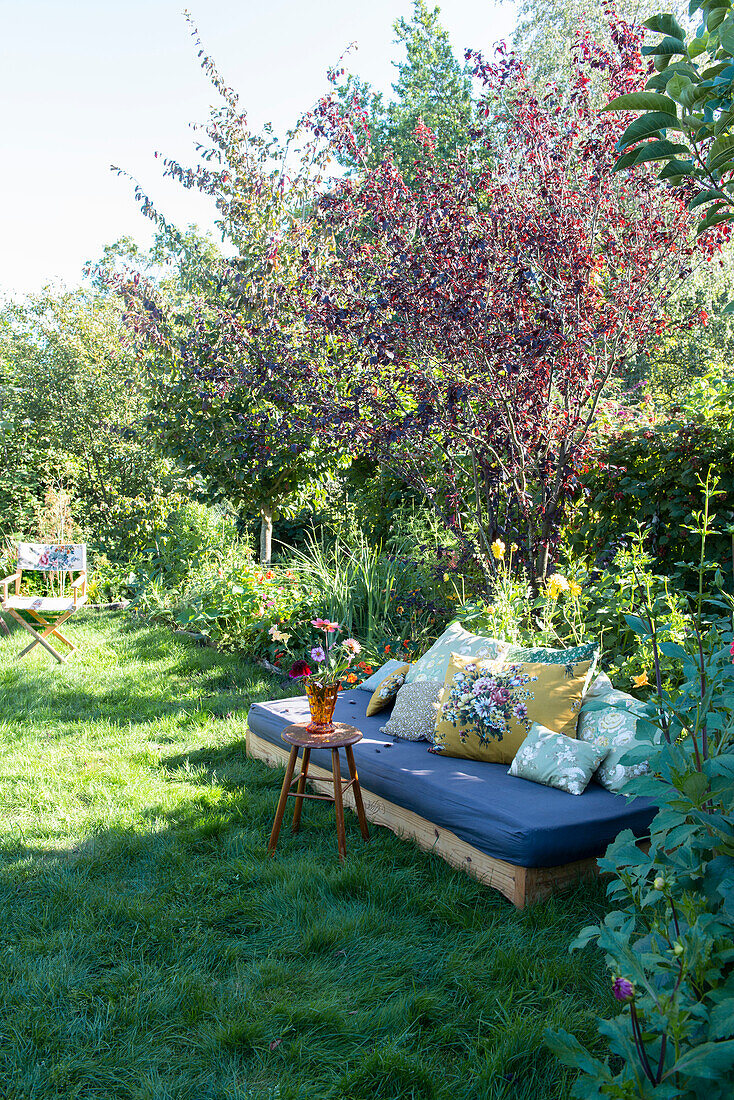 Gartenbereich mit blühenden Bäumen, Sofa und bunten Kissen