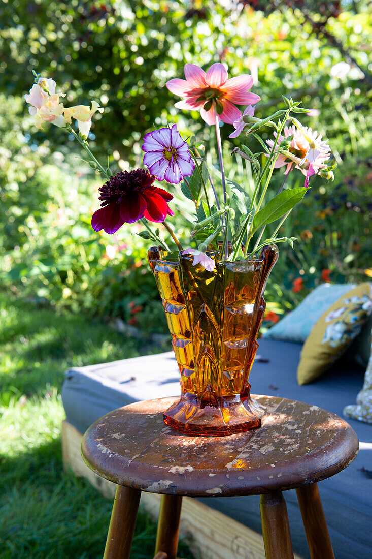 Bunte Sommerblumen in einer bernsteinfarbenen Vase auf Holzstuhl im Garten