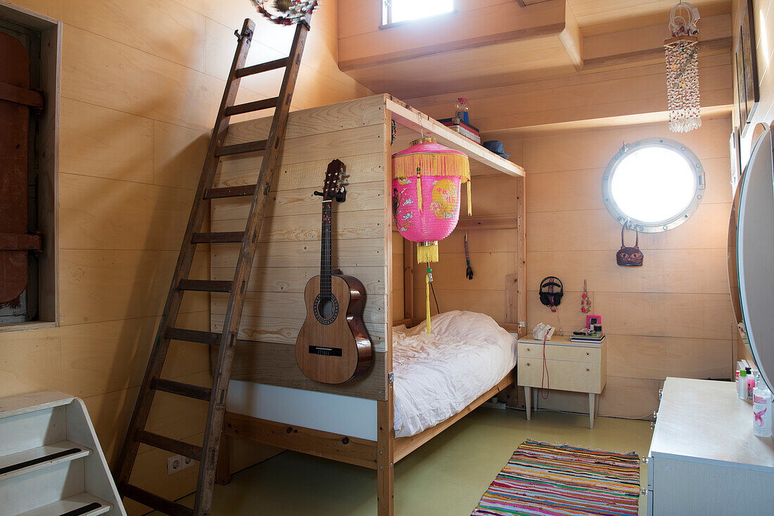 Wood-panelled children's room with four-poster bed, ladder and guitar