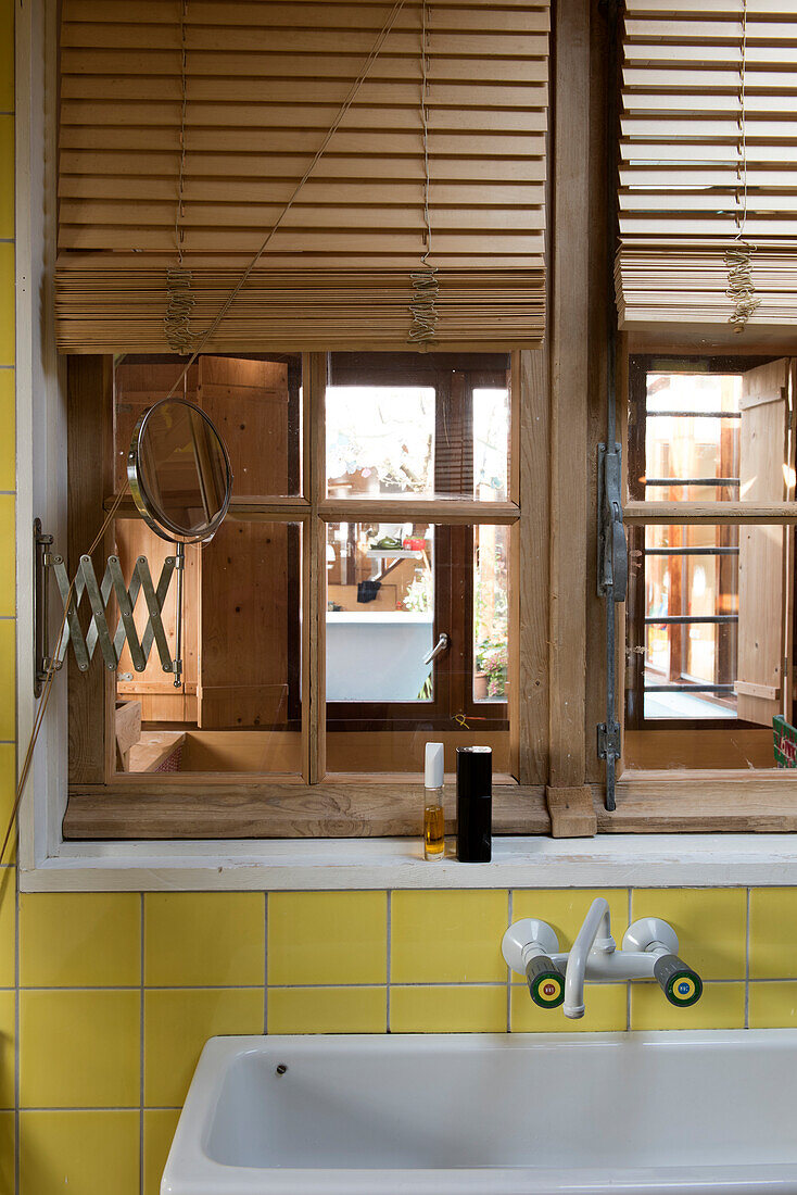 Wooden window with louvre blinds in the bathroom with yellow tiles