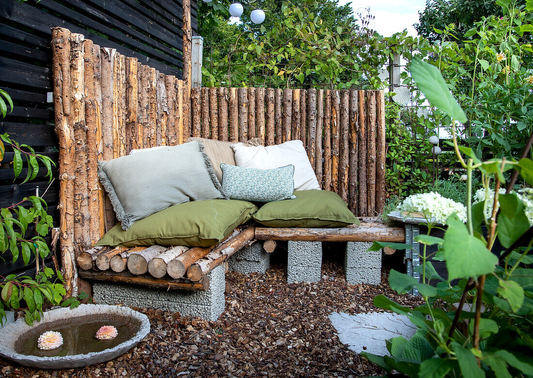 Corner sofa made from tree trunks and concrete blocks in a cosy garden corner