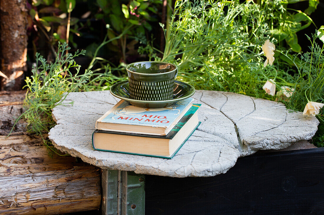 DIY-Tisch aus Beton mit Büchern und Tasse im Garten