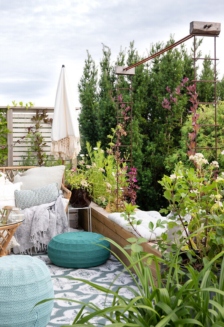 Roof terrace with raised bed and seating area made of rattan and knitted poufs