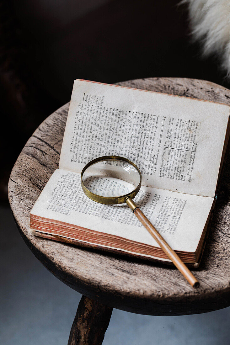 Altes Buch und Lupe auf Holzhocker