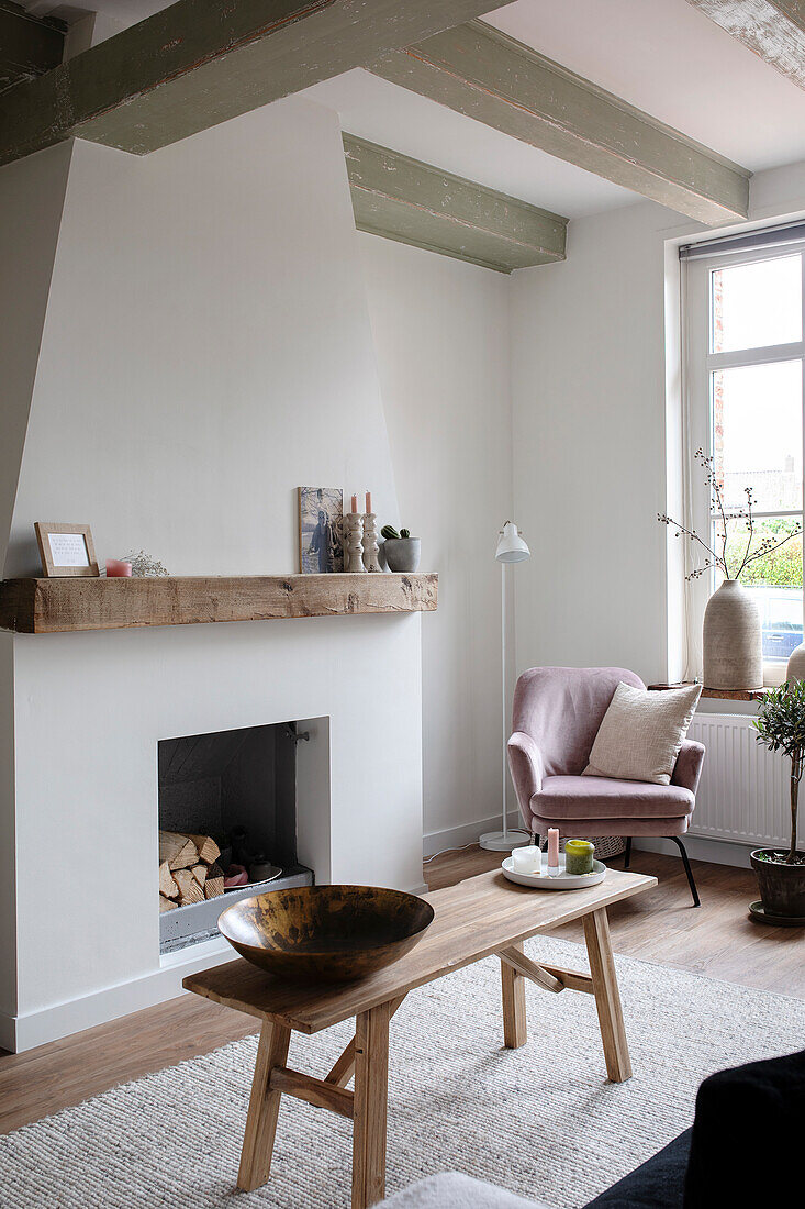 Living room with beamed ceiling and fireplace, pink armchairs and wooden table