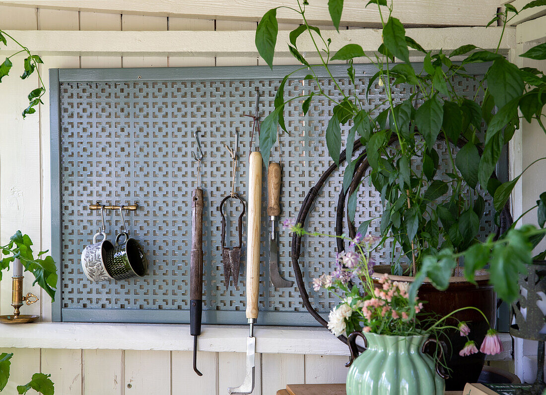 Wand mit Haken und Gartenutensilien, daneben eine Blumenvase und Pflanzen