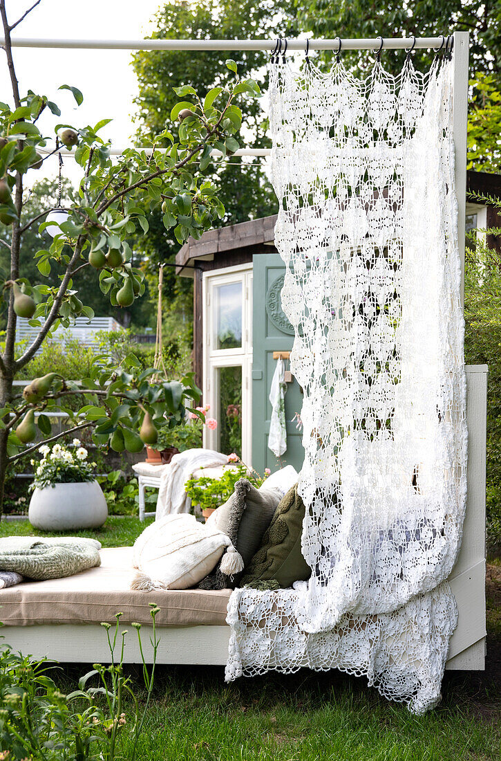 Sun bed with crocheted curtain and cushions in the garden