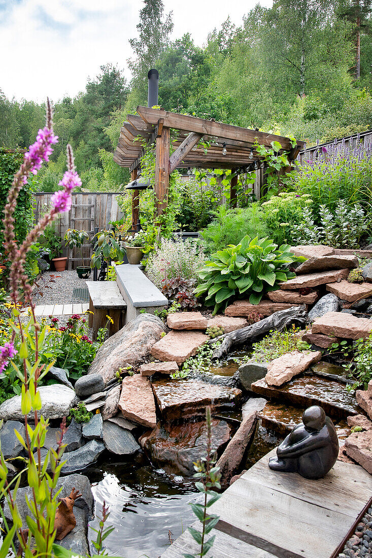 Garden with water feature, wooden pergola and lush planting in summer