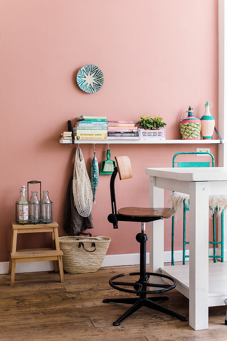 Living area with pink wall and wooden floor, decorated with colourful accessories