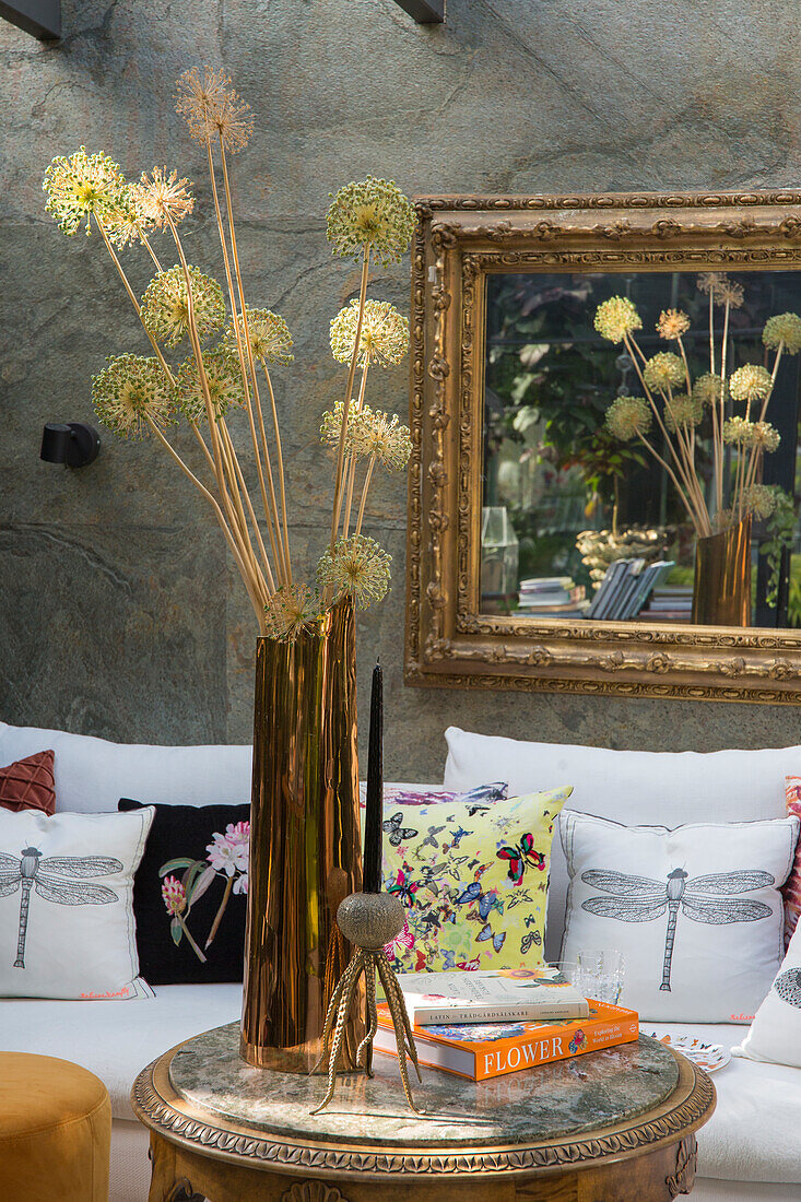 Round metal table with decorative objects and dried flowers in front of sofa