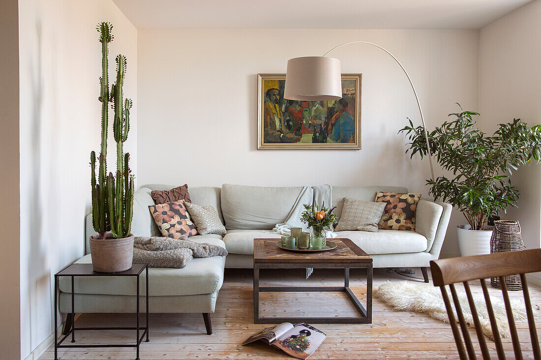 Living room in light colors with sofa, houseplants, painting and arc lamp