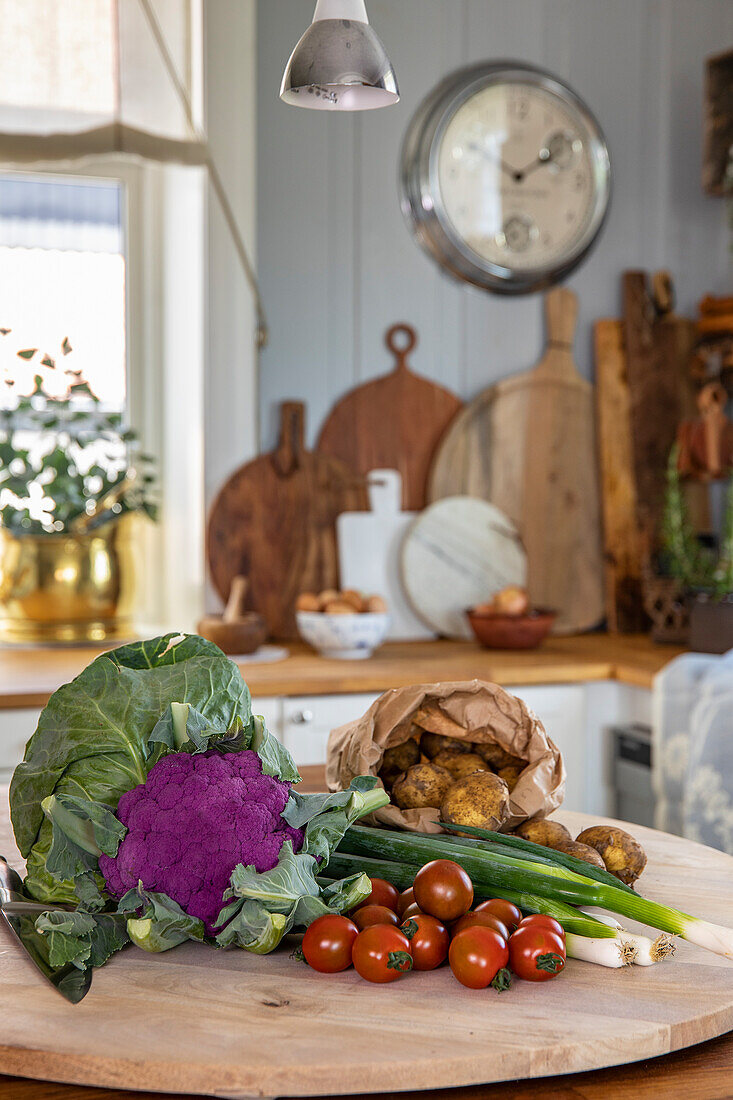 Frisches Gemüse auf Holzbrett in rustikaler Küche mit Wanduhr