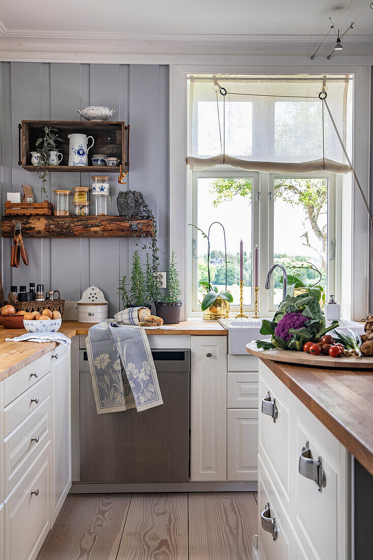 Küche im Landhausstil mit Kräutertöpfen und Gemüse auf Holzbrett