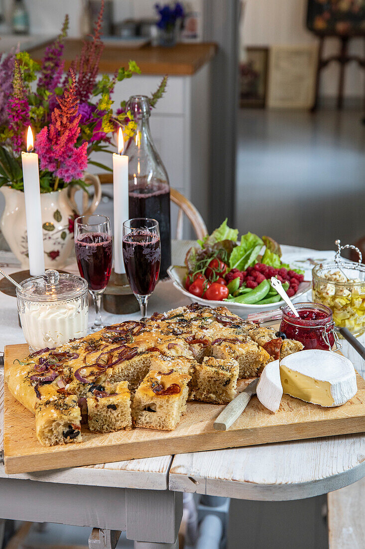 Gedeckter Tisch mit Käse, Gemüse, Marmelade und frisch gebackenem Kuchen