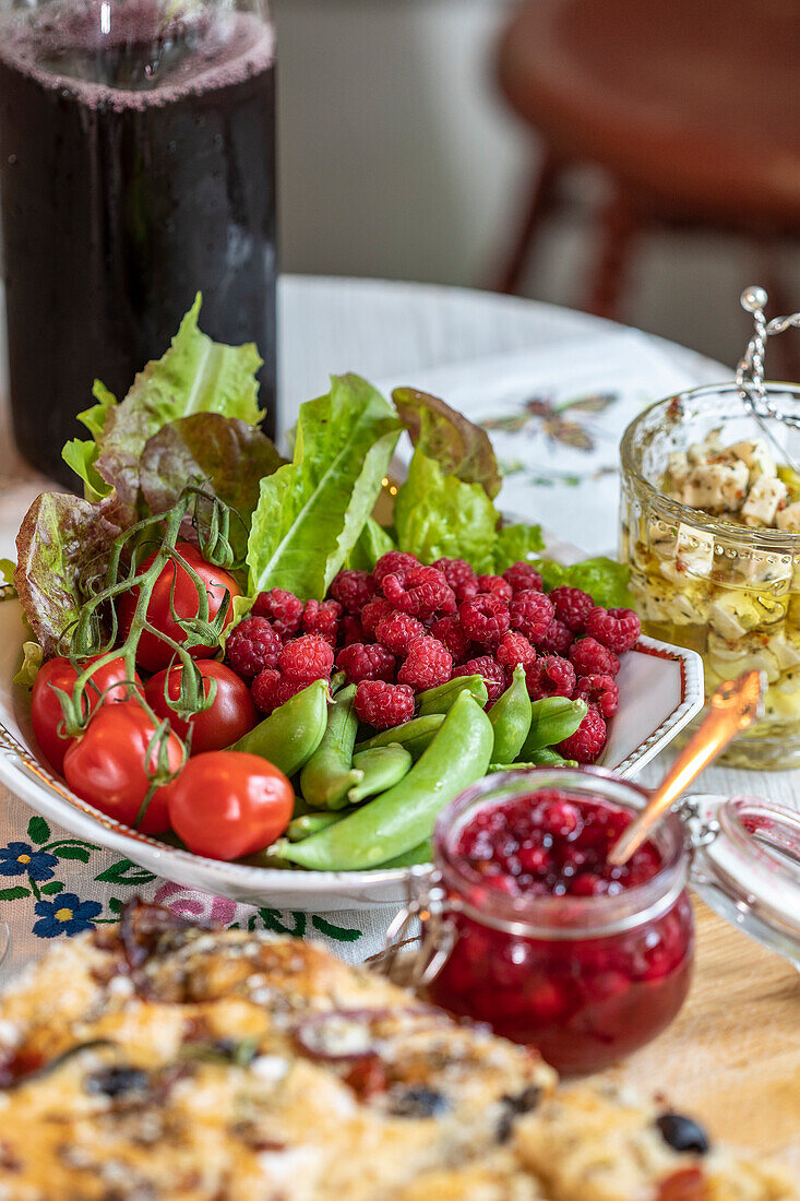 Raspberries, salad and vegetables, juice and homemade jam on the dining table