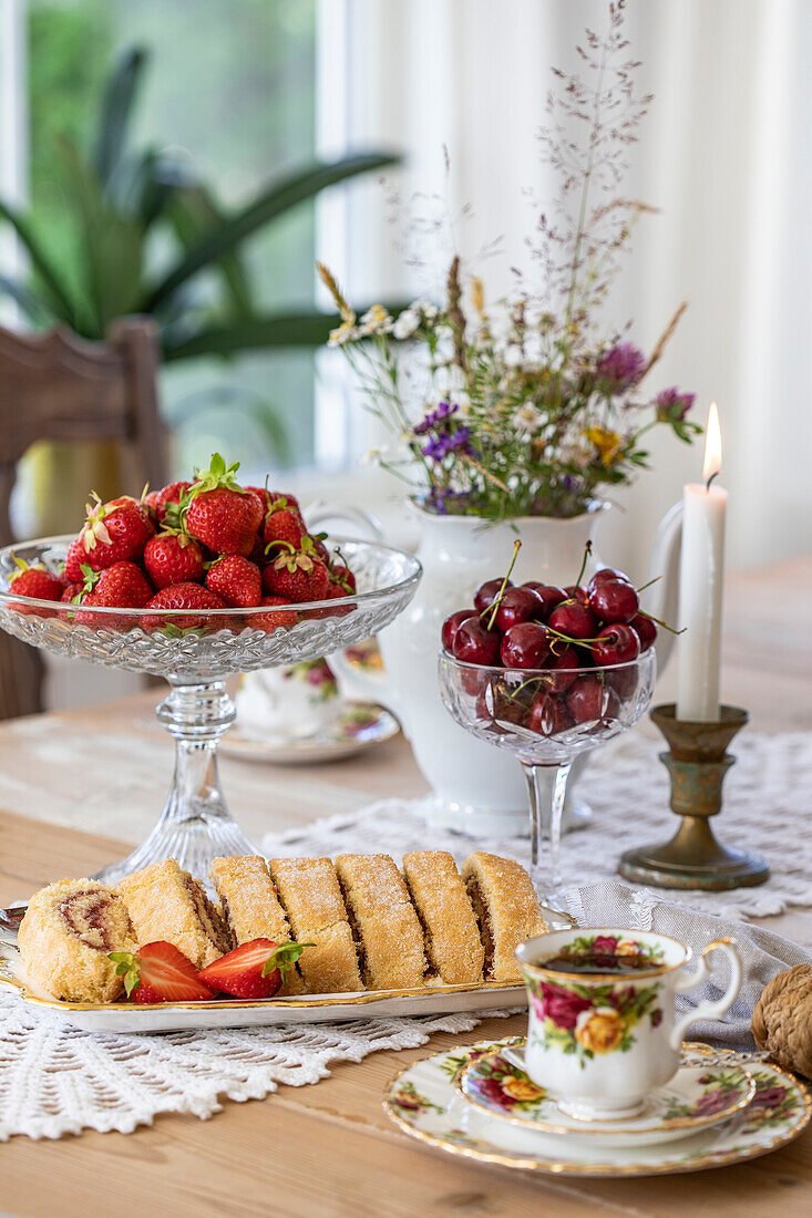 Gedeckter Tisch mit Erdbeeren, Kirschen, Kuchen, Blumen und Kerze