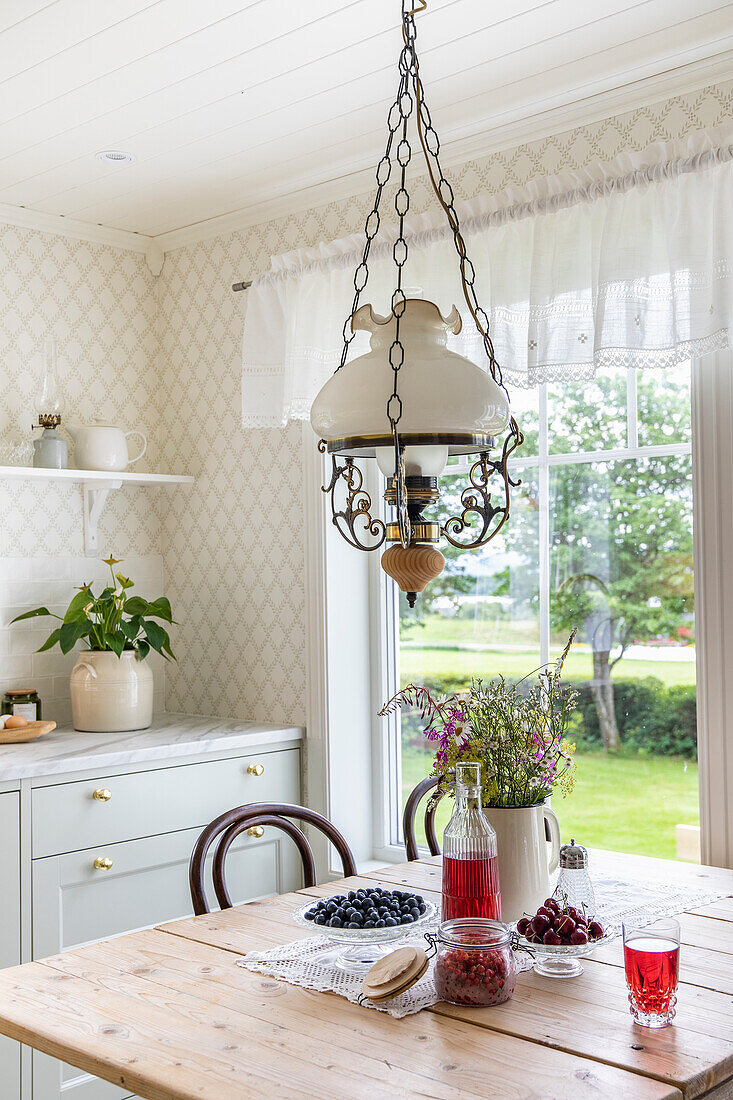 Hanging lamp over wooden table with summer flowers and fruit in country-style dining room