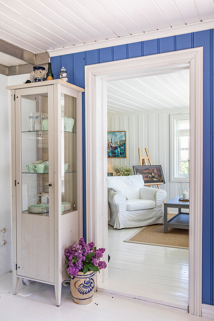 Helles Landhaus-Interieur mit blauer Wandvertäfelung und Vitrinenschrank