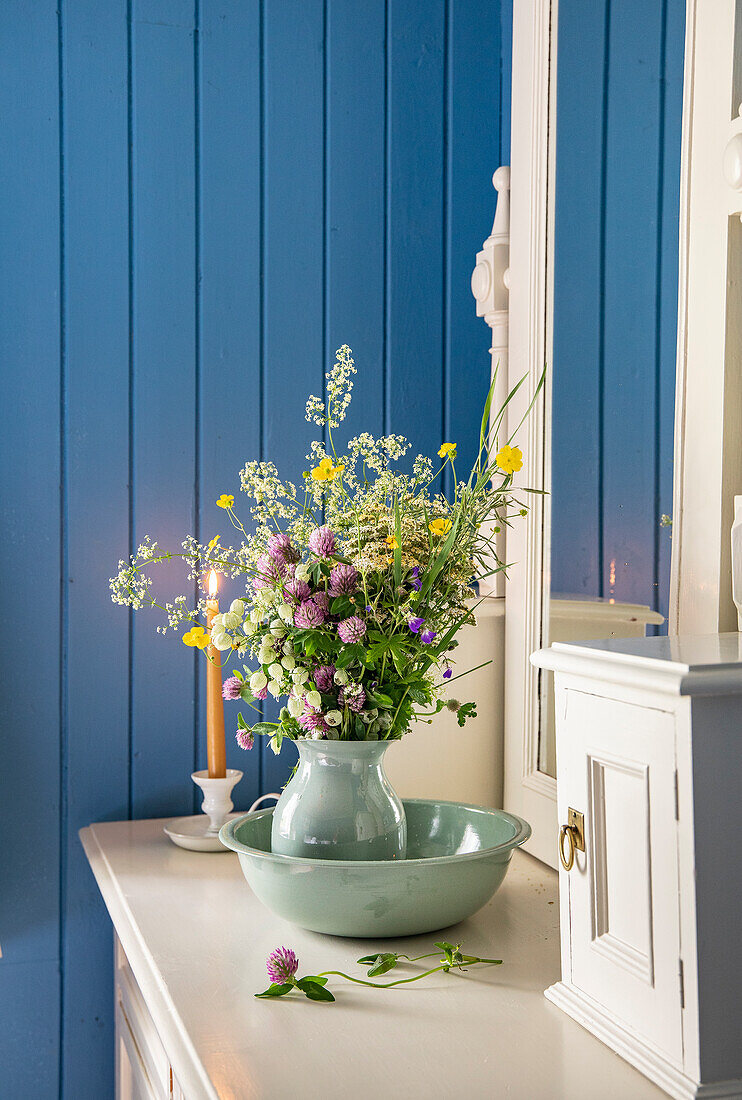 Vase mit Wildblumenstrauß auf einer weißen Kommode vor einer blauen Holzverkleidung