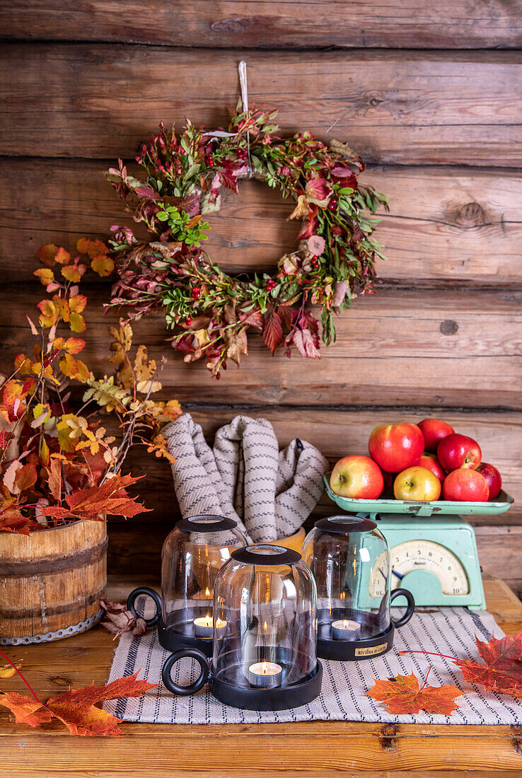 Autumn decorations with wreath, lanterns and apples on a rustic wooden wall