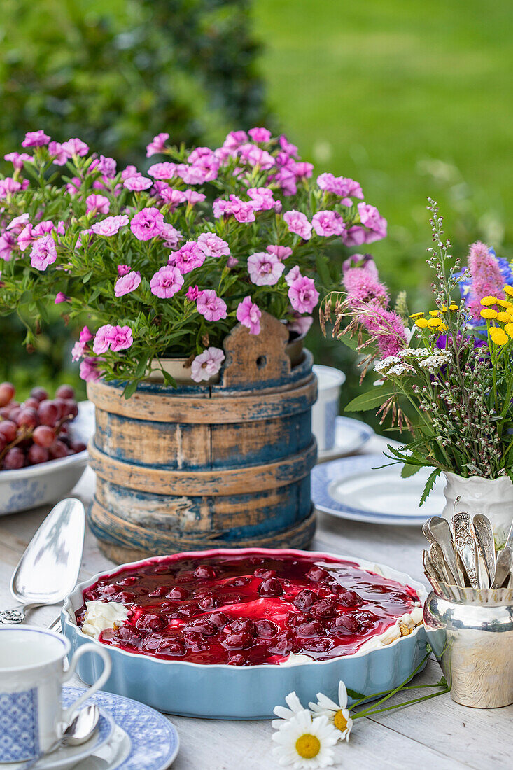 Garden table with cake, floral decorations and crockery in summer