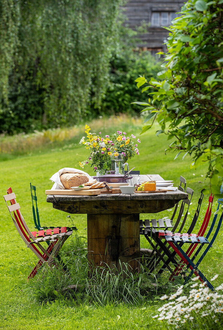 Garden table with colorful chairs and summer flowers in a meadow