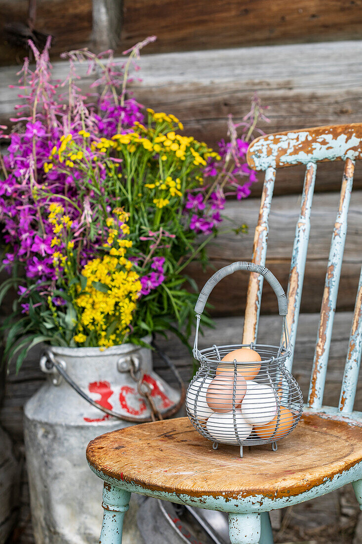 Fresh eggs in a wire basket on a rustic chair, wildflowers in an old milk churn