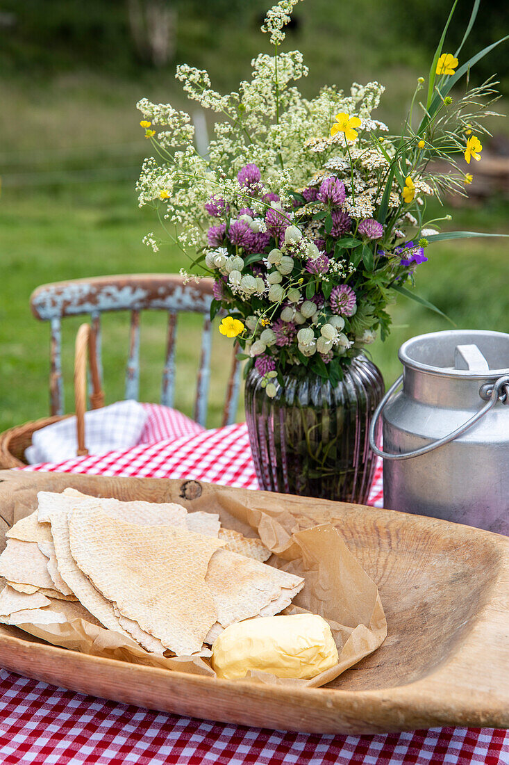 Frühlingsblumenstrauß in Glasvase auf Picknicktisch mit Butter und Knäckebrot