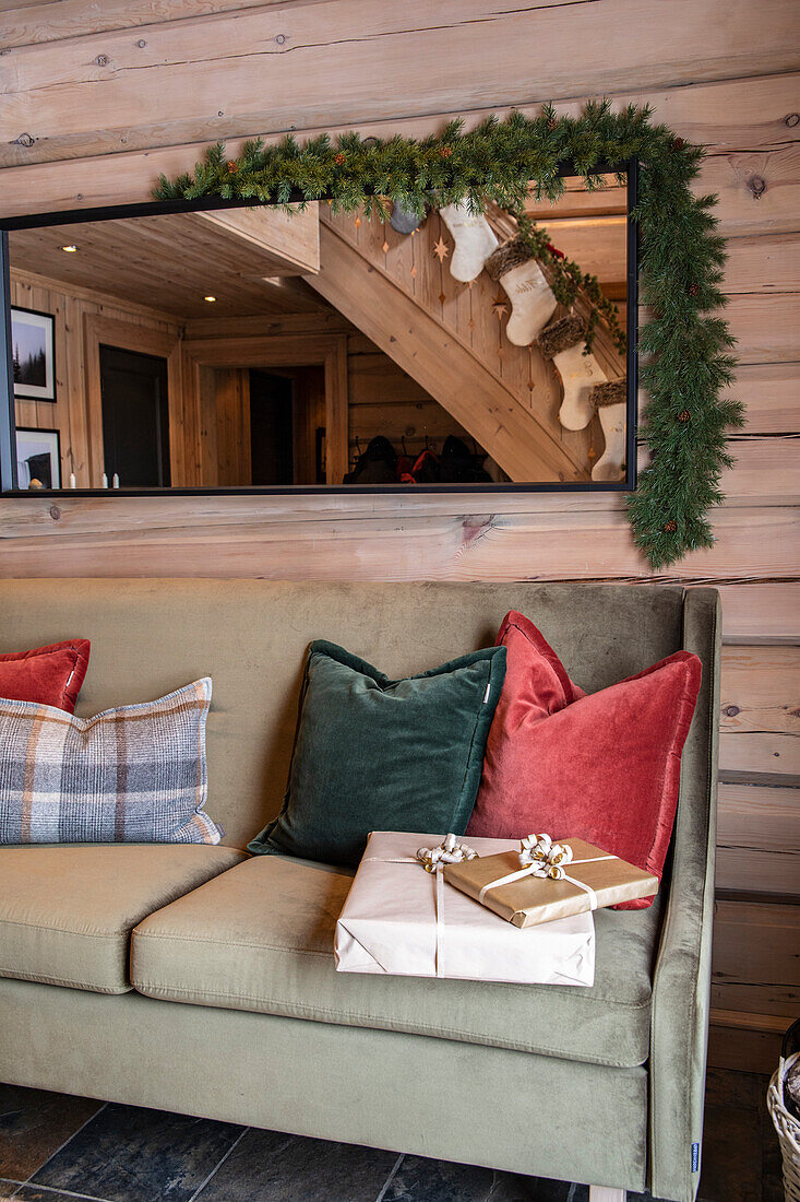 Rustic living room with Christmas decorations on a wooden wall and presents on a sofa