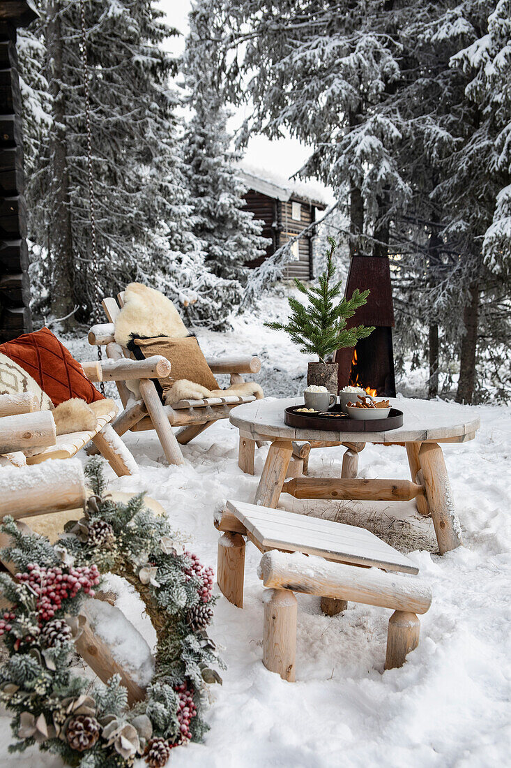 Winterliche Gartenecke mit Holzmöbeln, Feuerstelle, Fellen und Weihnachtsdekoration