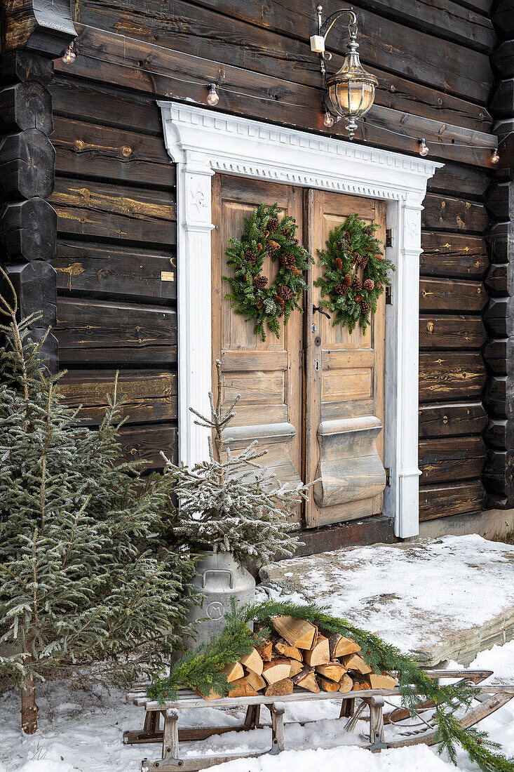 Eingangstür eines rustikalen Hauses mit weihnachtlichen Kränzen und winterlicher Dekoration