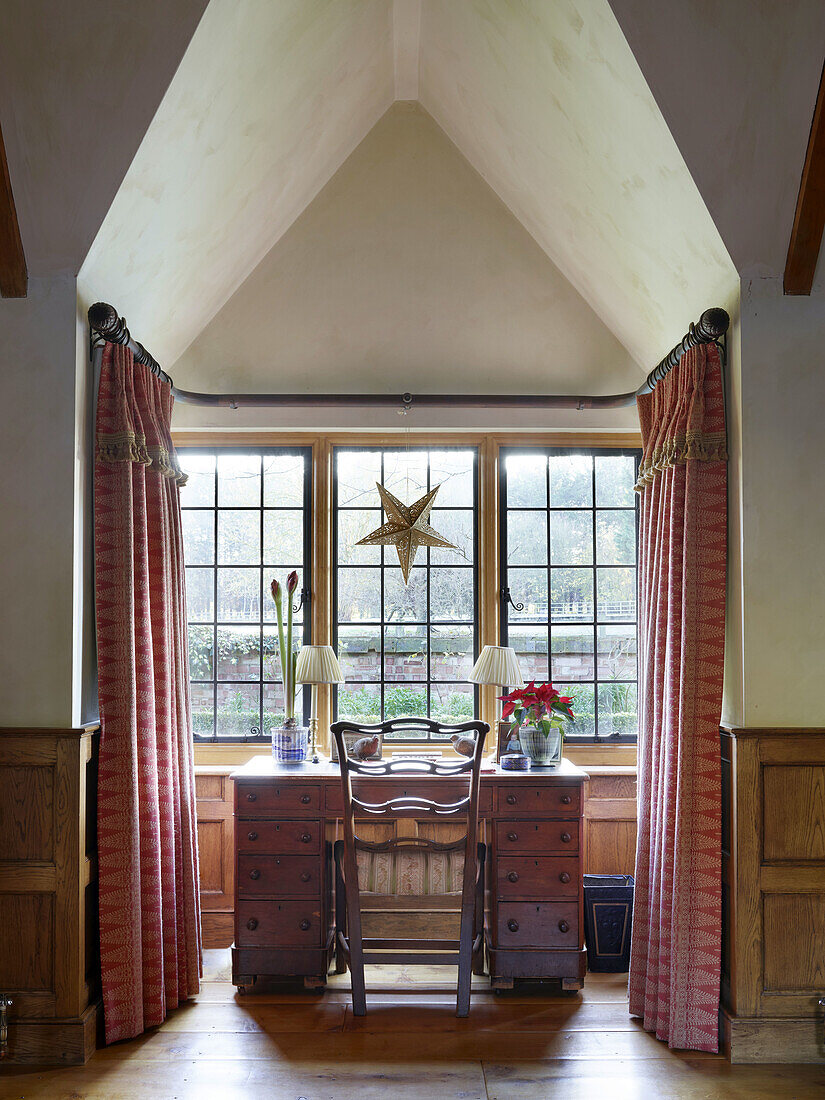 Sprossenfenster mit Stern-Dekoration und Blumenvasen auf Schreibtisch