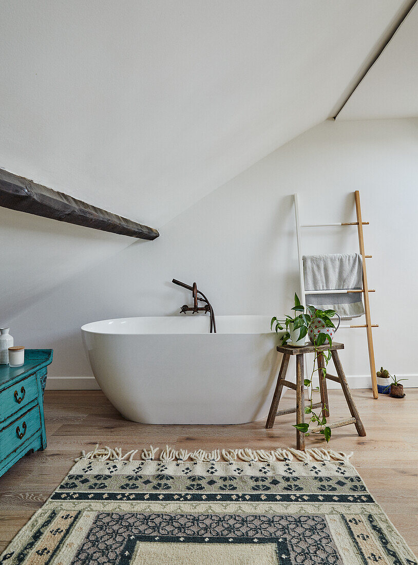 Freistehende Badewanne in einem Dachgeschoss mit Sichtbalken und handgeknüpftem Teppich