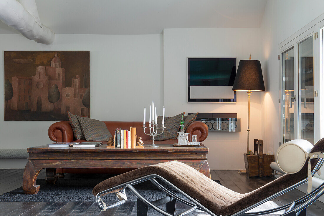 Living room with brown leather sofa, candlestick on wooden table and designer lounger