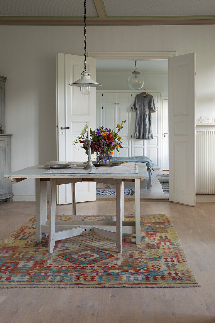 Esszimmer im Landhausstil mit gemustertem Teppich und Blumenstrauß auf Holztisch