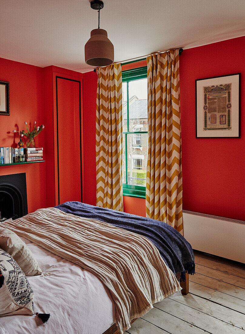 Bedroom with bold red walls, green window frame and patterned chevron curtains