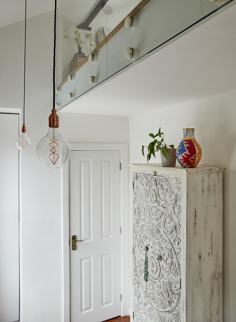 Hallway with vintage cupboard and modern pendant lights in a hallway, gallery above with glass balustrade