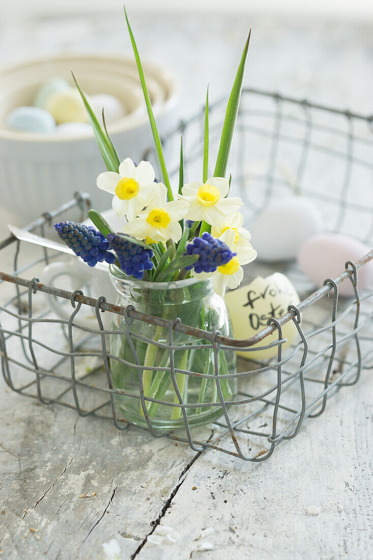 Spring flowers in jar, egg shell and Easter eggs in wire basket
