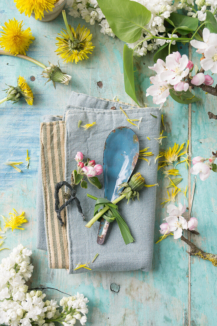 Napkin with letter made of string, tin spoon with grass decoration, between dandelion, lilac and apple blossom