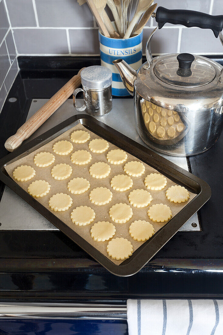 Cut-out cookies on baking tray next to teapot in rustic kitchen