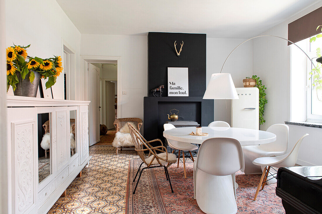 Dining room with round table, different chairs and sunflowers on white sideboard