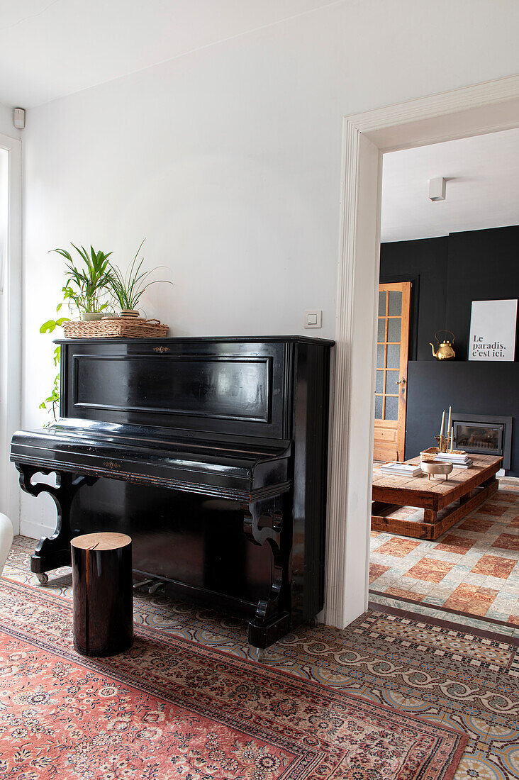 Black piano in the passageway between two rooms with oriental carpet