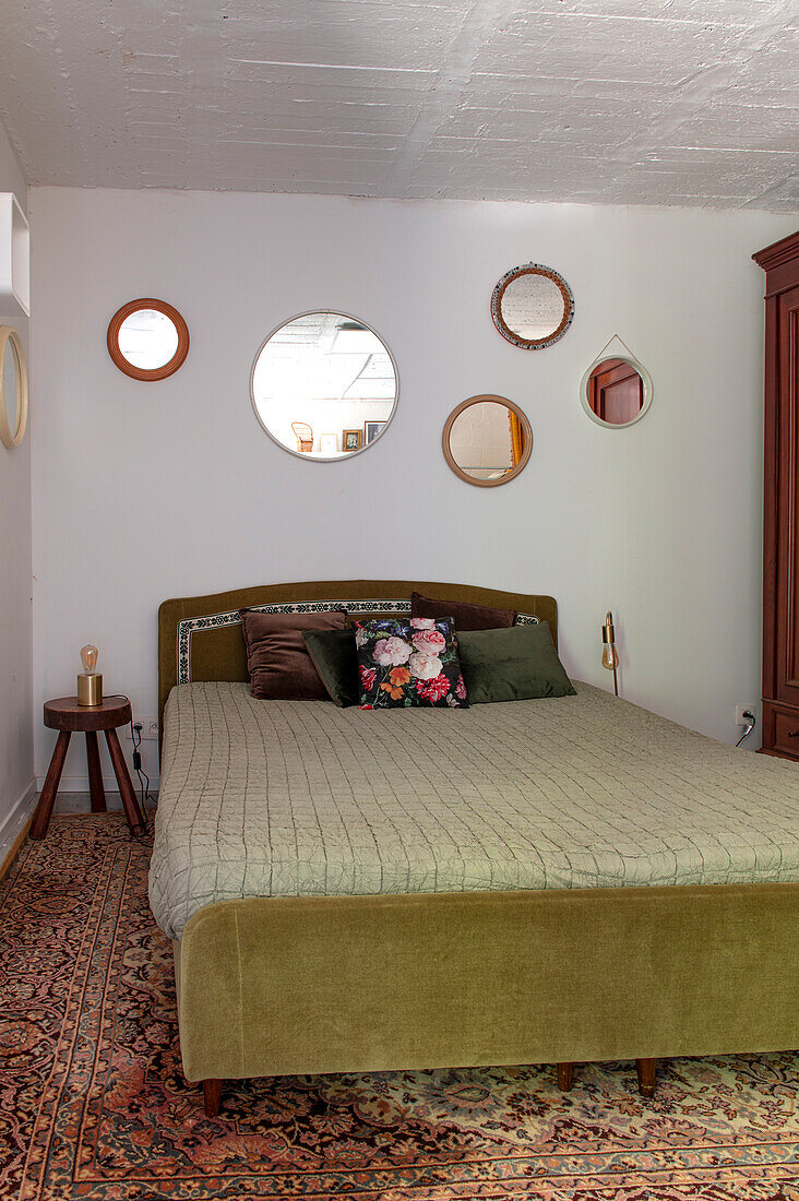 Old-fashioned bedroom with olive green upholstered bed, patterned carpet and round mirrors on the wall